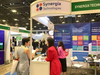 Visitors explore the Synergix Technologies booth at a trade show, examining ERP software solutions and business management displays.