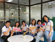 A team of Synergix employees smiles together in a modern office meeting room during a casual team gathering.
