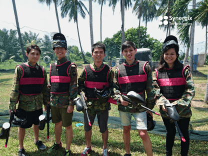 Five people wearing matching black and pink tactical vests stand together outdoors in a tropical setting.