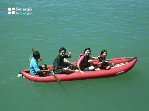 Four people paddle together in a red kayak on turquoise water, demonstrating teamwork and collaboration.